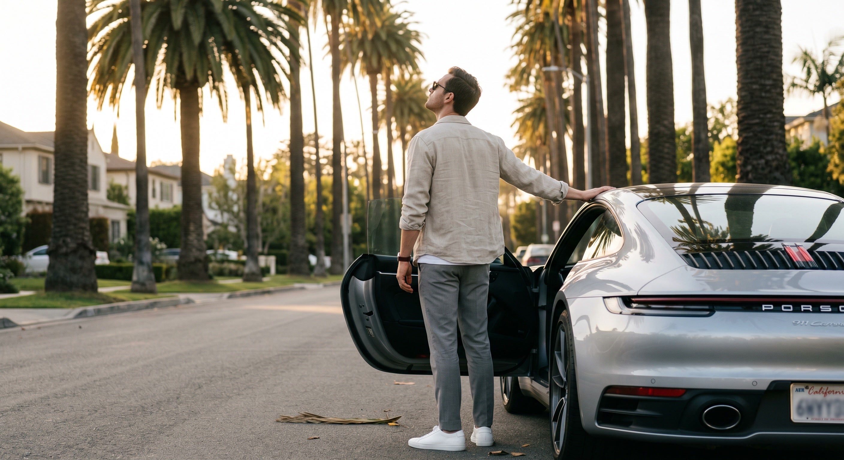 A VIRILANT man beside his Porsche on a palm-lined street